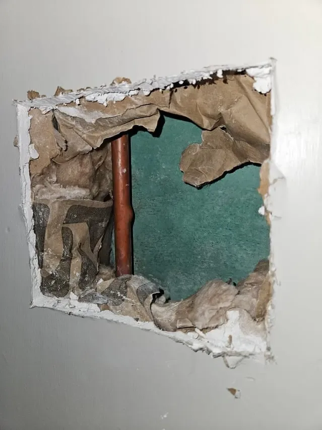 Copper pipe exposed through a broken section of plaster wall