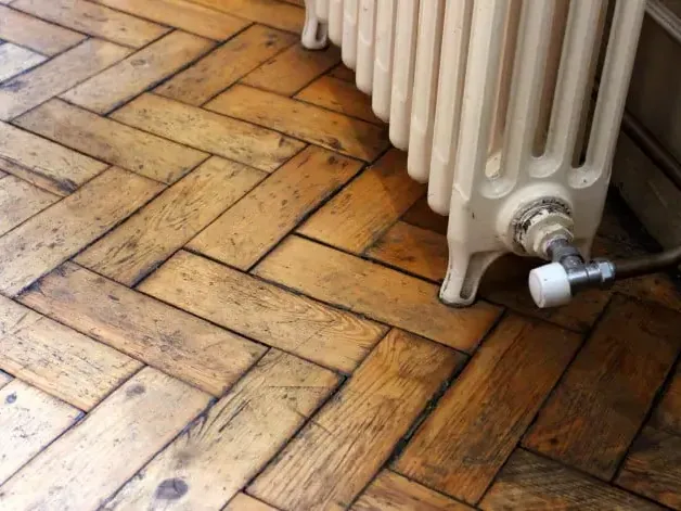 Water-stained herringbone wood flooring beneath a radiator